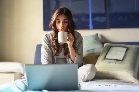 Woman sitting on bed with laptop and cup of tea